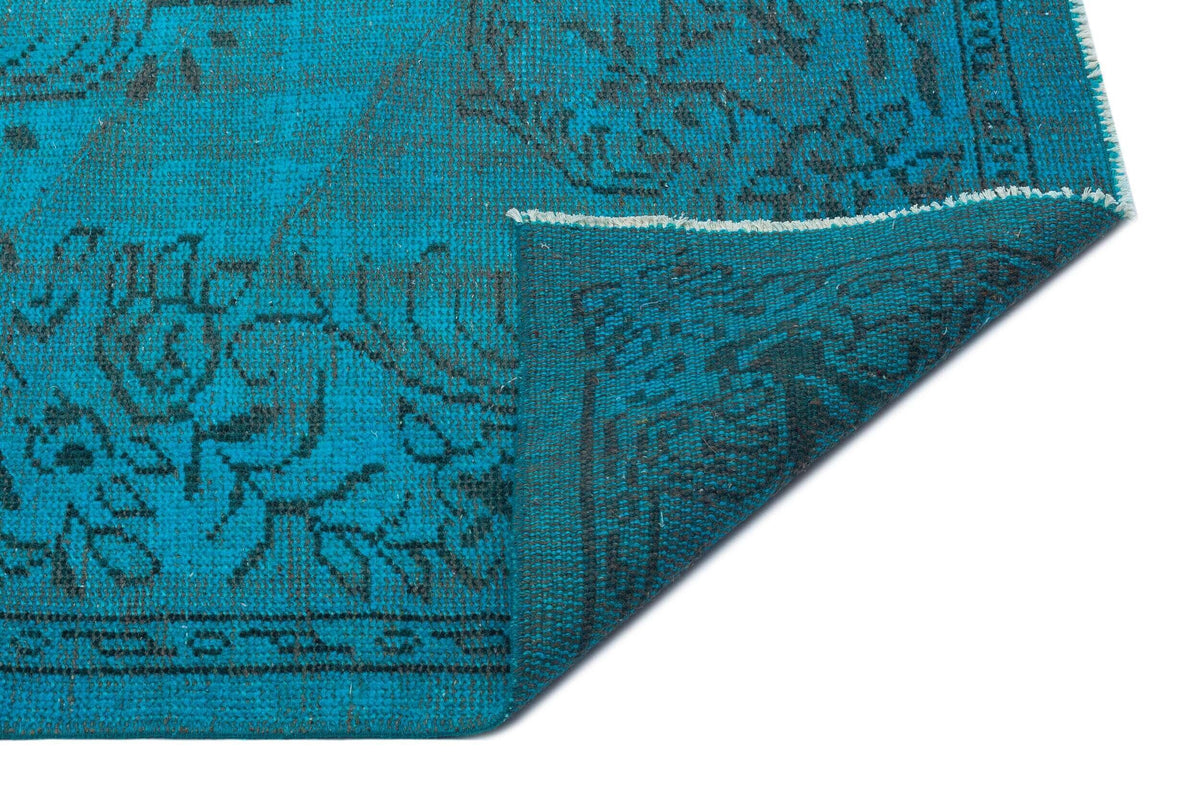 Teal and black rug with a distressed floral medallion pattern, shown with a corner folded over to reveal the backing.
