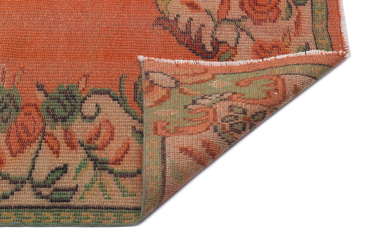 Burnt orange rug with a floral pattern in green and tan, shown with a corner folded over on a white background.