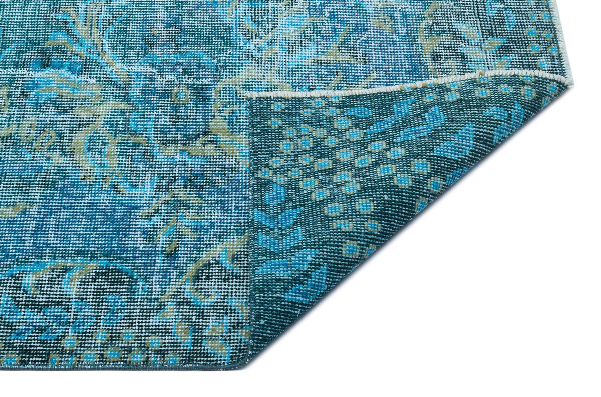 Blue and teal distressed rug with a traditional floral medallion pattern, shown with a corner folded over.