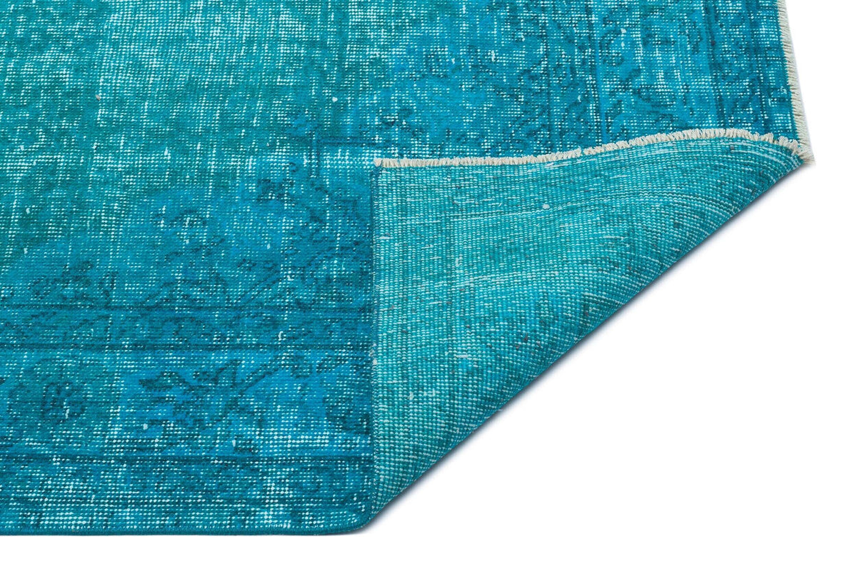 Distressed turquoise rug with a faded traditional pattern and a folded corner showing the woven backing.