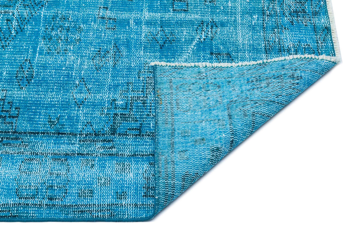 Bright blue distressed rug with a faded geometric pattern and a folded corner showing the woven backing.