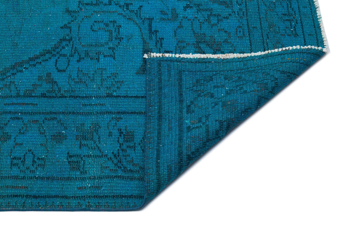 Teal blue rug with a dark, distressed traditional medallion pattern, shown with a corner folded over on a white background.