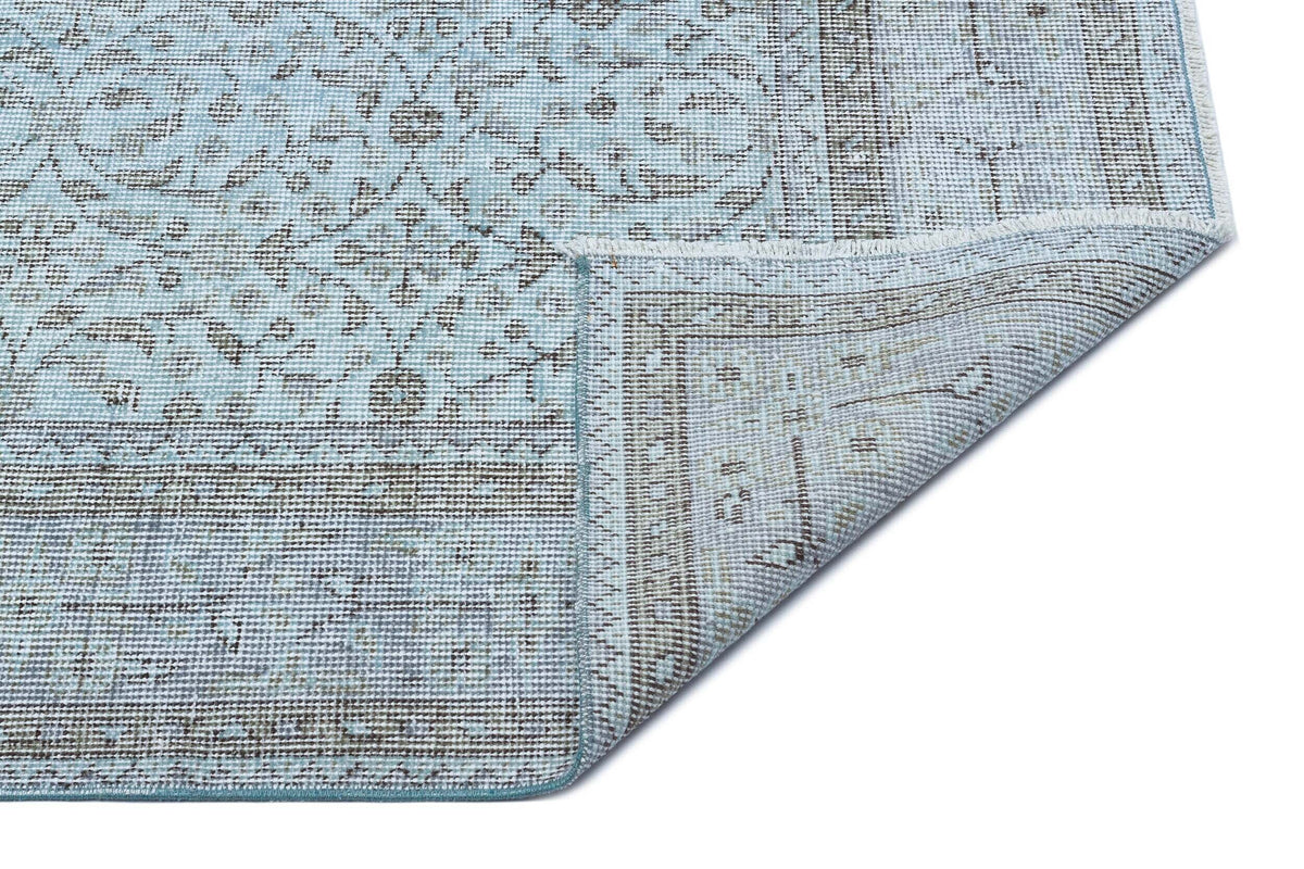 Light blue and grey traditional medallion rug with a folded corner showing the woven backing on a white background.