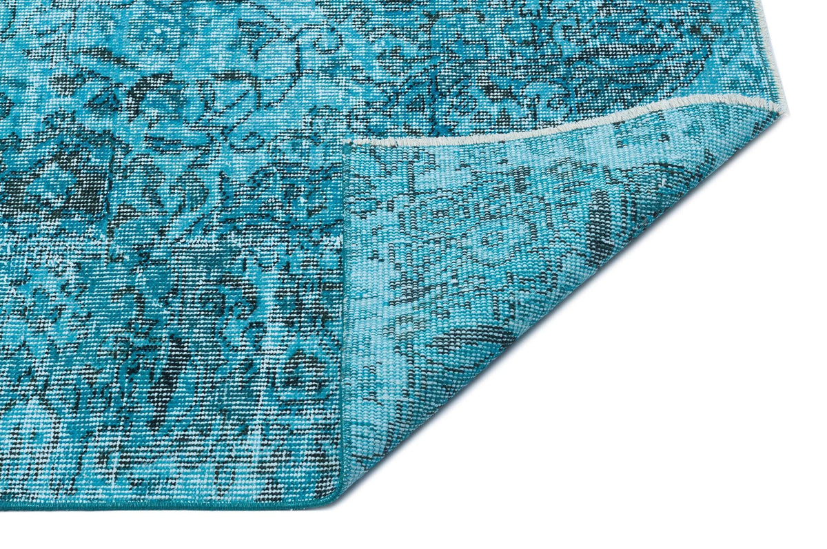 Turquoise and black distressed medallion pattern rug with a folded corner on a white background.