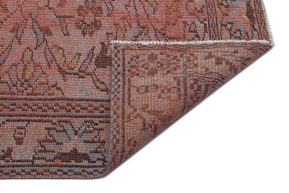 Terracotta and brown vintage-style rug with a distressed floral pattern, shown with a corner folded over.