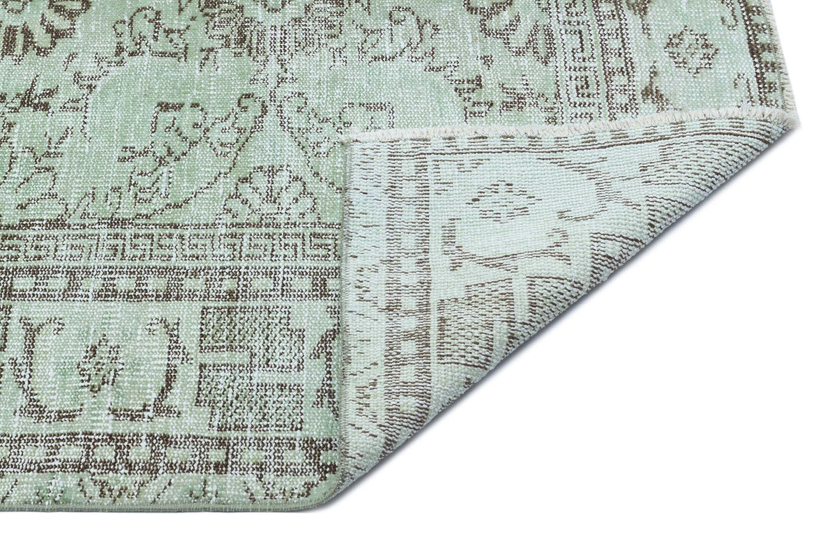 Sage green and brown distressed traditional rug with a folded corner showing the underside texture.