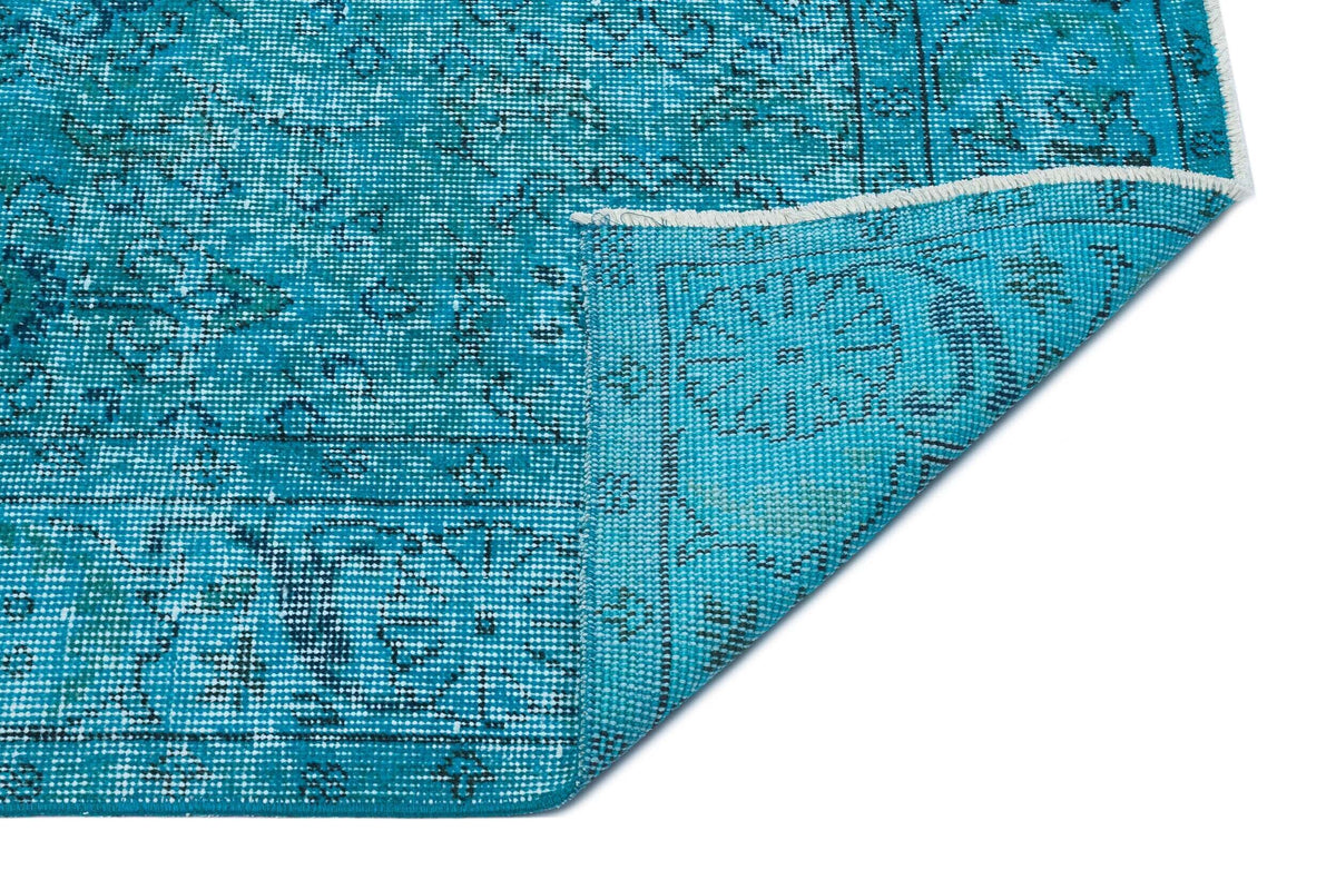 Turquoise and black distressed traditional medallion rug with a folded corner on a white background.