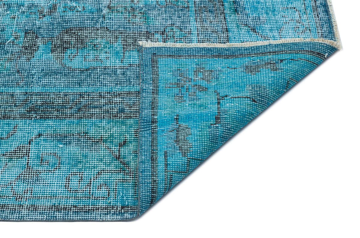 Bright blue distressed rug with a black traditional medallion pattern, shown with a corner folded over on white.