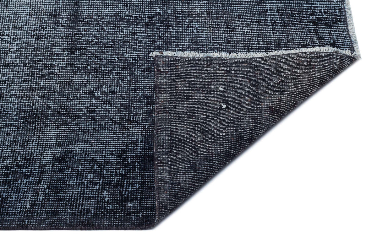 Charcoal and navy blue distressed area rug with a folded corner revealing the dark woven backing and fringe edge.
