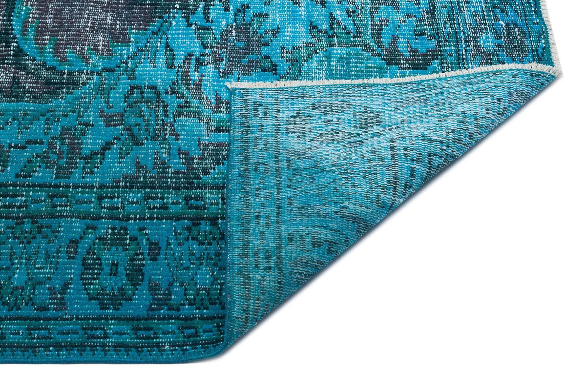 Turquoise and black distressed medallion rug with a folded corner showing the textured underside.