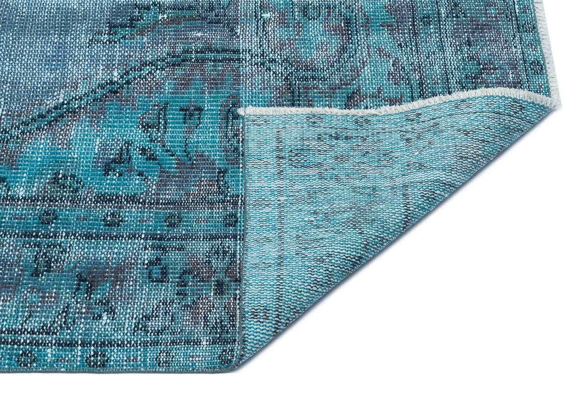 Teal and charcoal distressed medallion rug with a folded corner revealing the woven backing on a white background.