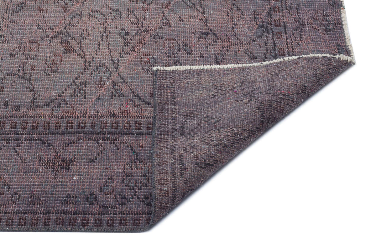 Dark purple distressed rug with a faded floral pattern and a folded corner showing the textured backing.