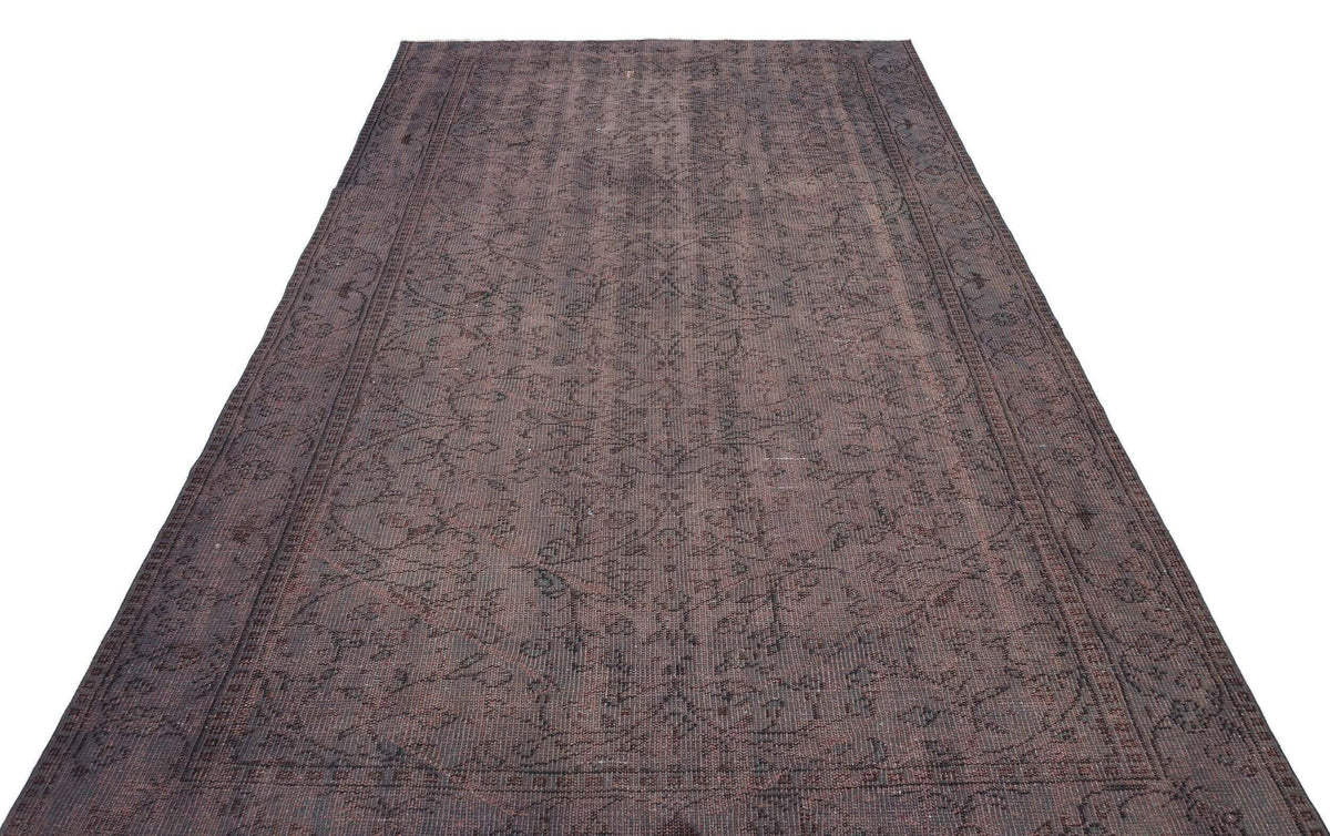 Dark brown distressed rug with a faded traditional floral pattern and a bordered edge on a white background.