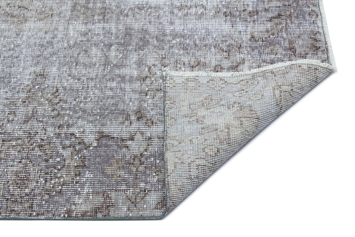 Grey and taupe distressed traditional rug with a faded medallion pattern, shown with a corner folded over.