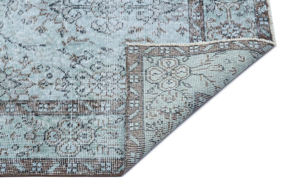 Light blue and brown distressed rug with a traditional floral medallion pattern, shown with a corner folded over.