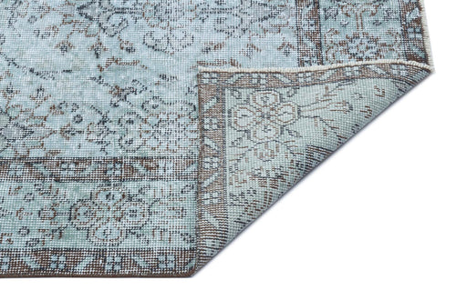 Load image 1 in gallery view. Light blue and brown distressed rug with a traditional floral medallion pattern, shown with a corner folded over.