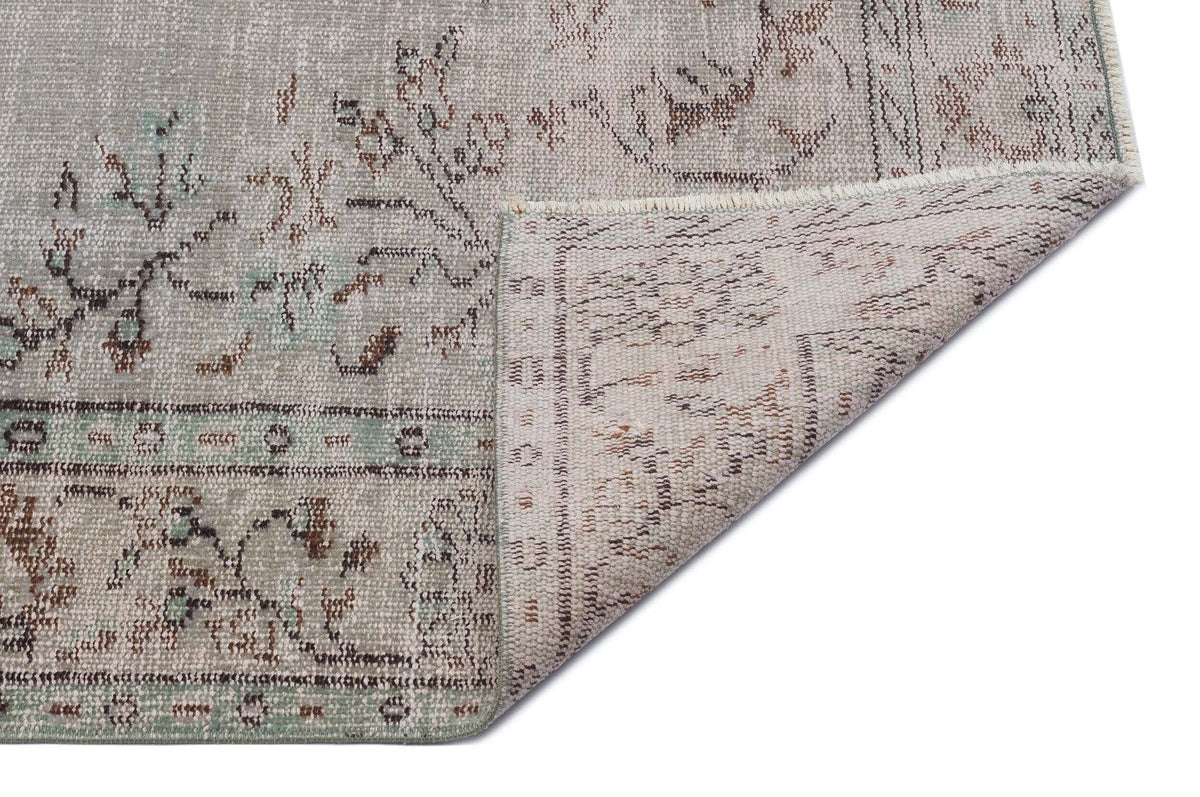 Distressed grey and sage green rug with a faded floral pattern, shown with a corner folded over on a white background.
