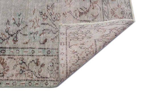 Load image 1 in gallery view. Distressed grey and sage green rug with a faded floral pattern, shown with a corner folded over on a white background.