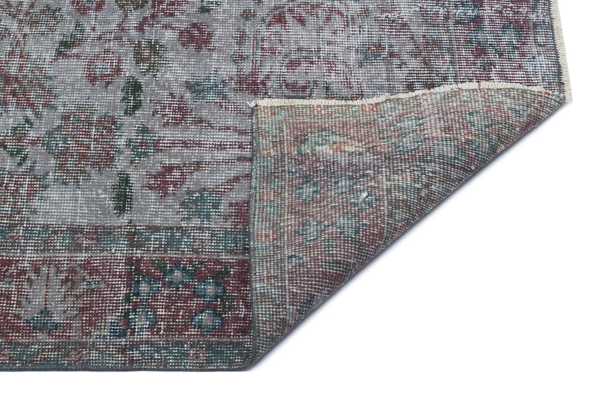 Distressed grey, burgundy, and teal traditional floral rug with a folded corner showing the reverse side.