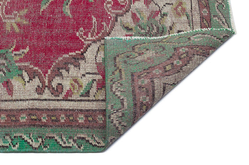 Load image 1 in gallery view. Distressed red and green traditional rug with a floral medallion pattern, shown with a corner folded over.
