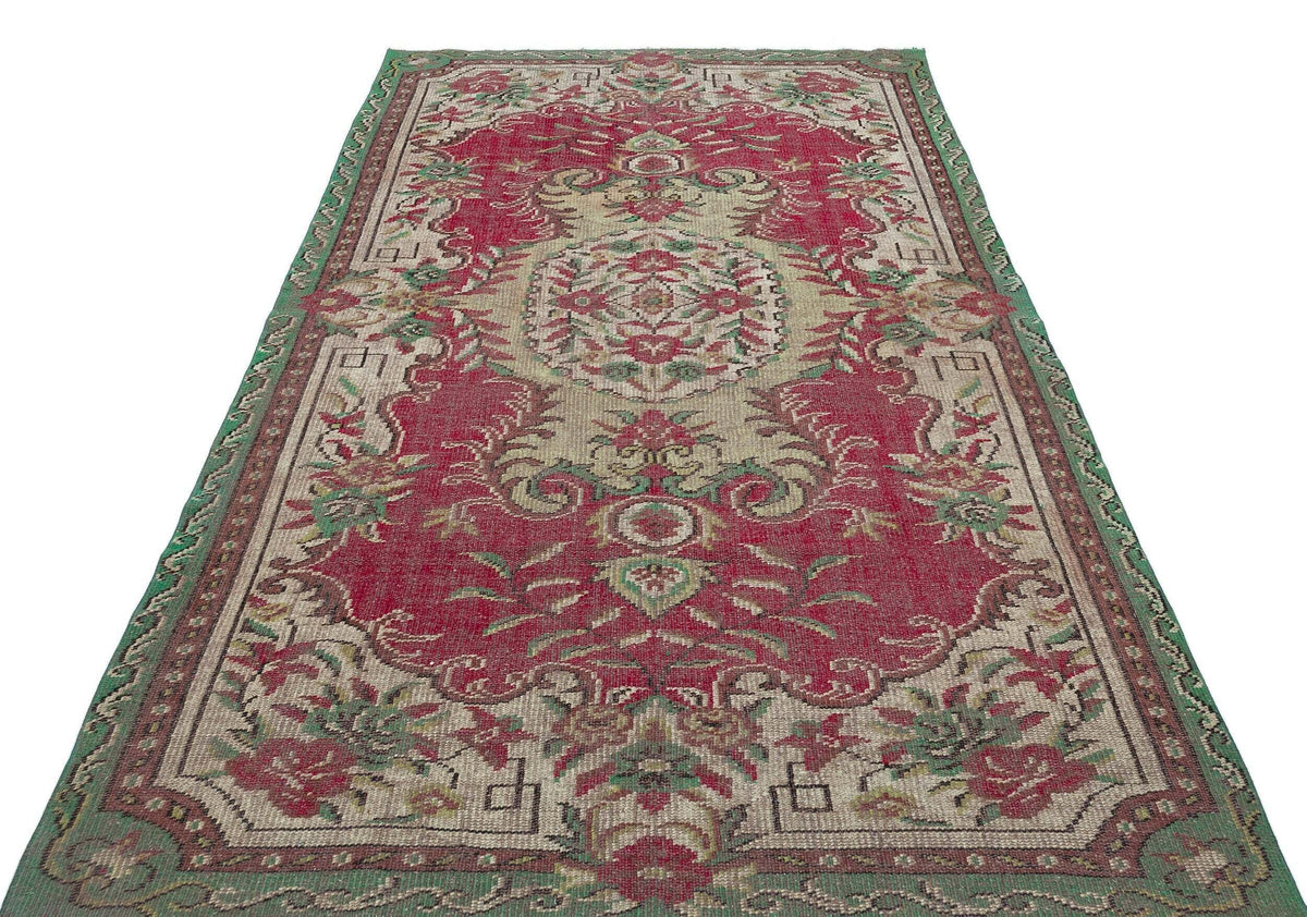 Red and beige vintage-style rug with a central floral medallion, ornate borders, and green accents on a white background.