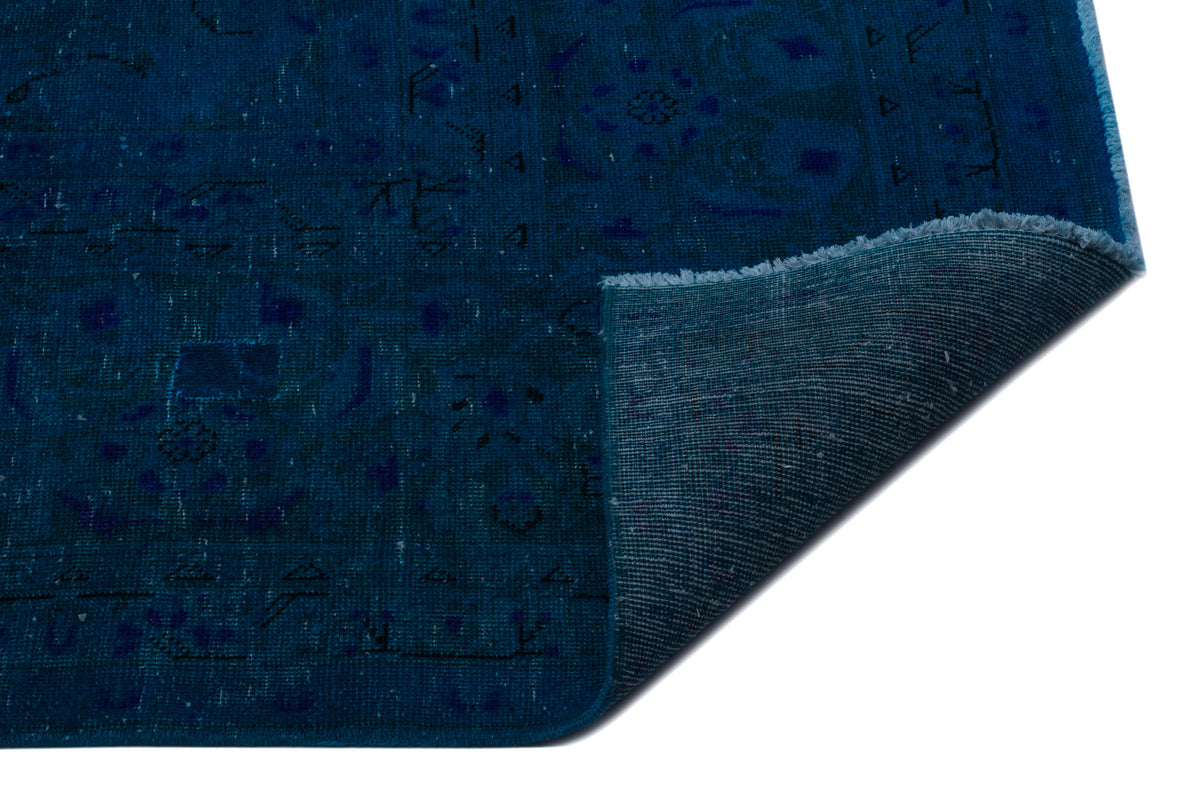 Deep blue rug with a faded traditional medallion pattern and a folded corner showing the woven backing.