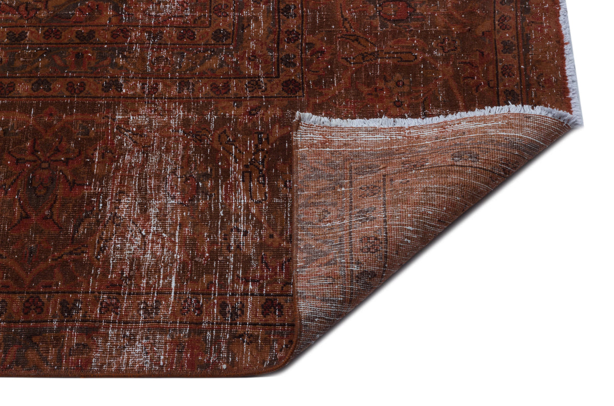 Distressed rust-colored rug with a traditional Persian-style pattern and a folded corner showing the underside.