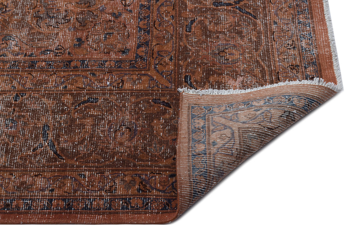 Distressed rust and navy traditional Persian-style rug with a folded corner revealing the woven backing.