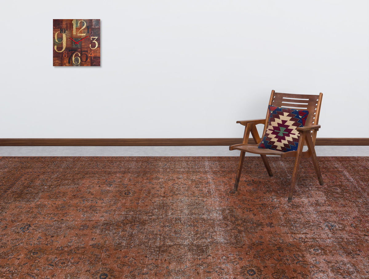 Distressed rust-colored traditional rug with a faded floral pattern, styled in a room with a wooden chair and wall clock.