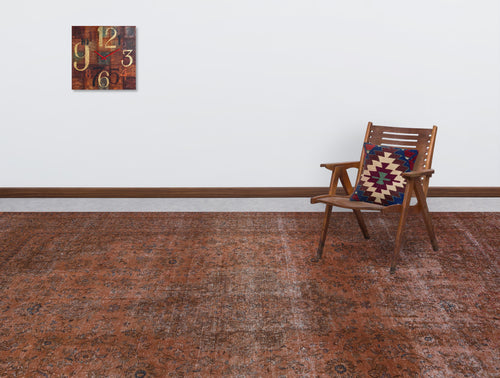 Load image 1 in gallery view. Distressed rust-colored traditional rug with a faded floral pattern, styled in a room with a wooden chair and wall clock.