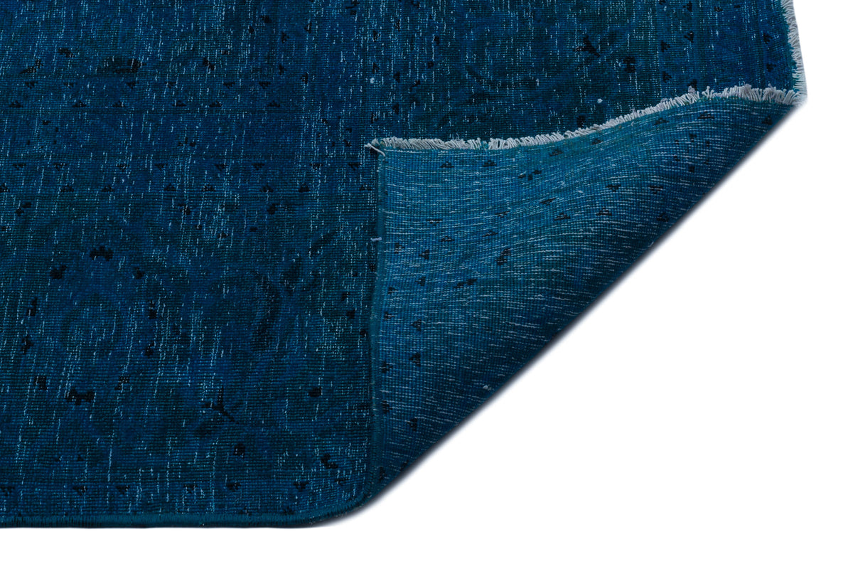 Deep blue distressed rug with small black geometric motifs and a folded corner showing the underside.