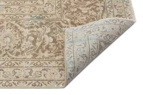 Load image 1 in gallery view. Beige and tan distressed traditional rug with a floral medallion pattern and a folded corner, isolated on white.