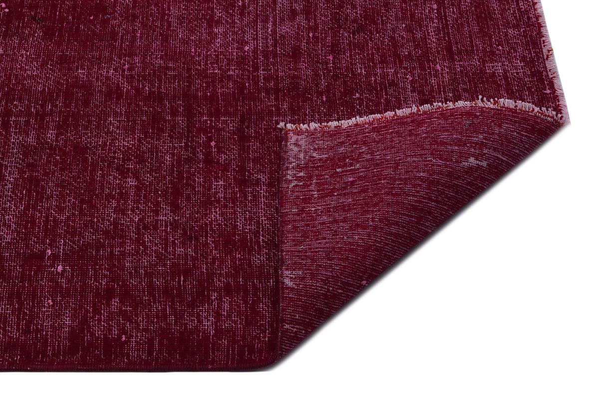 Deep burgundy rug with a distressed, textured finish and a folded corner showing the underside.