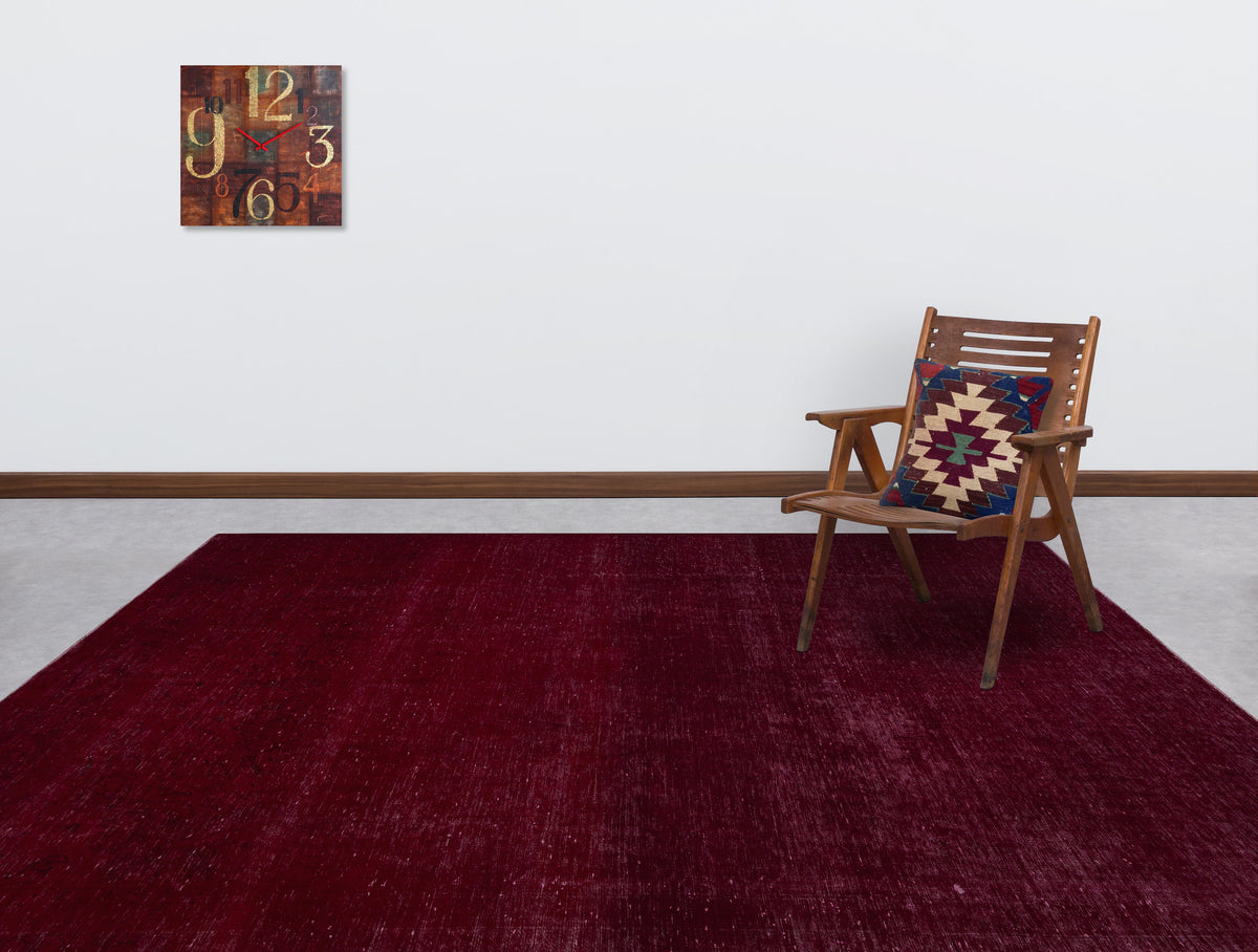 Solid deep red rug with a subtle distressed texture, styled in a room with a wooden chair and wall clock.