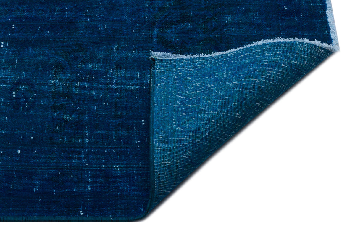 Deep blue distressed rug with a folded corner revealing a lighter teal backing and fringed edge on a white background.