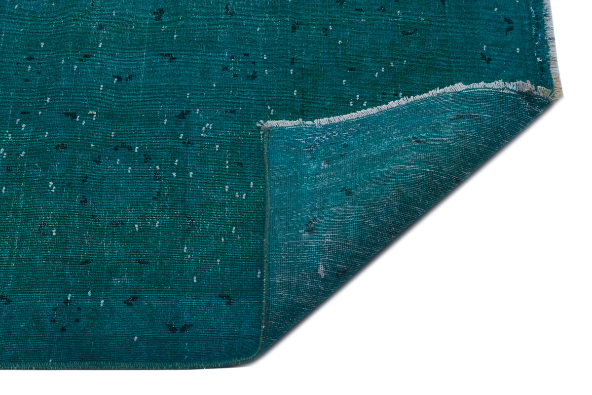 Teal distressed rug with a white speckled pattern and a folded corner showing the woven backing on a white background.