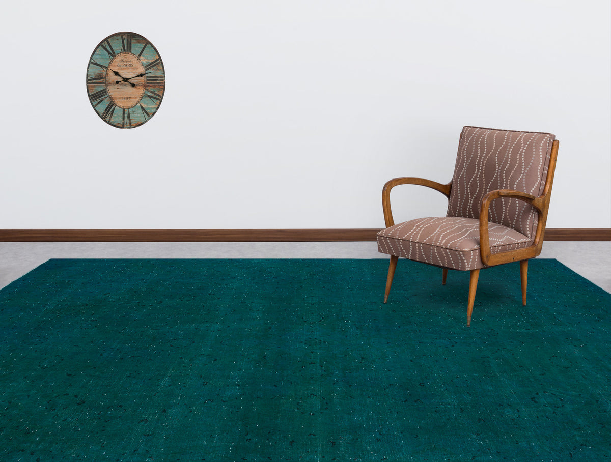 Solid teal rug with a subtle distressed texture, styled in a room with a patterned armchair and wall clock.