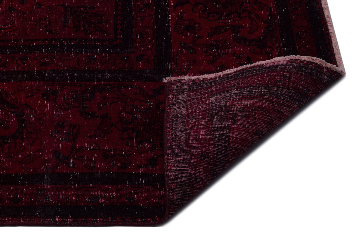 Deep red and black distressed rug with a traditional floral pattern, shown with a corner folded over.