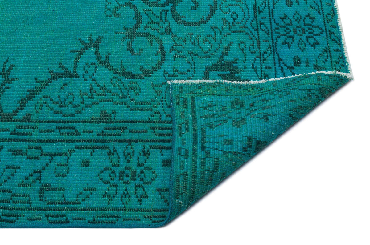 Teal rug with a black traditional floral medallion pattern, shown with a corner folded over on a white background.