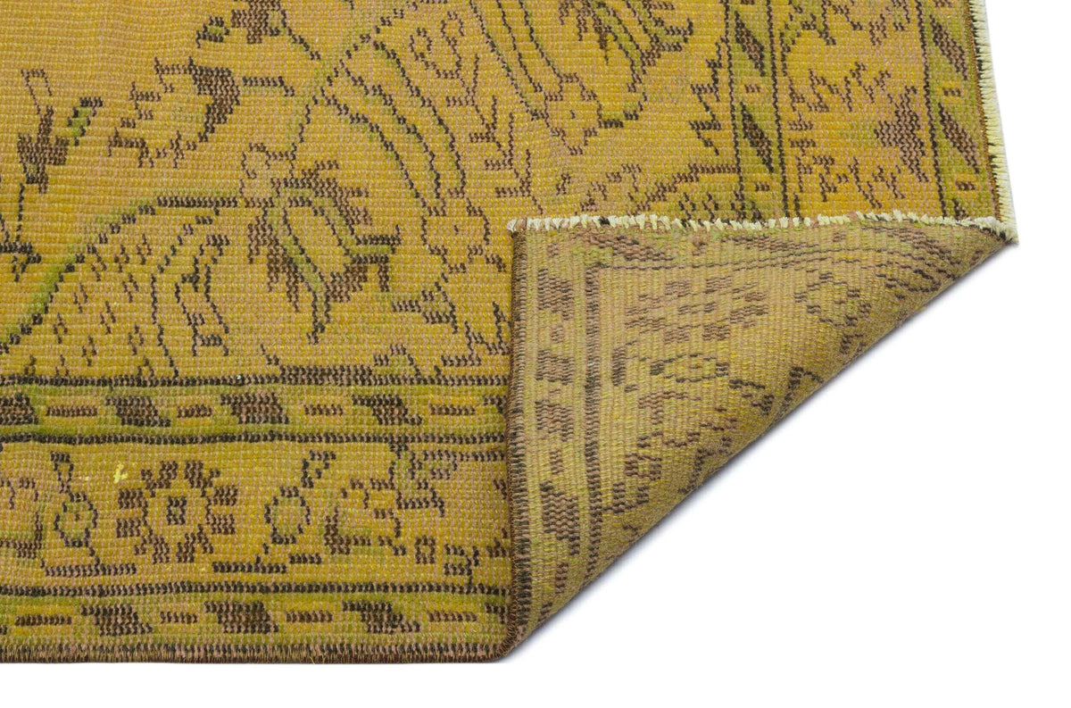 Mustard yellow and olive green vintage-style rug with a distressed floral medallion pattern and a folded corner.