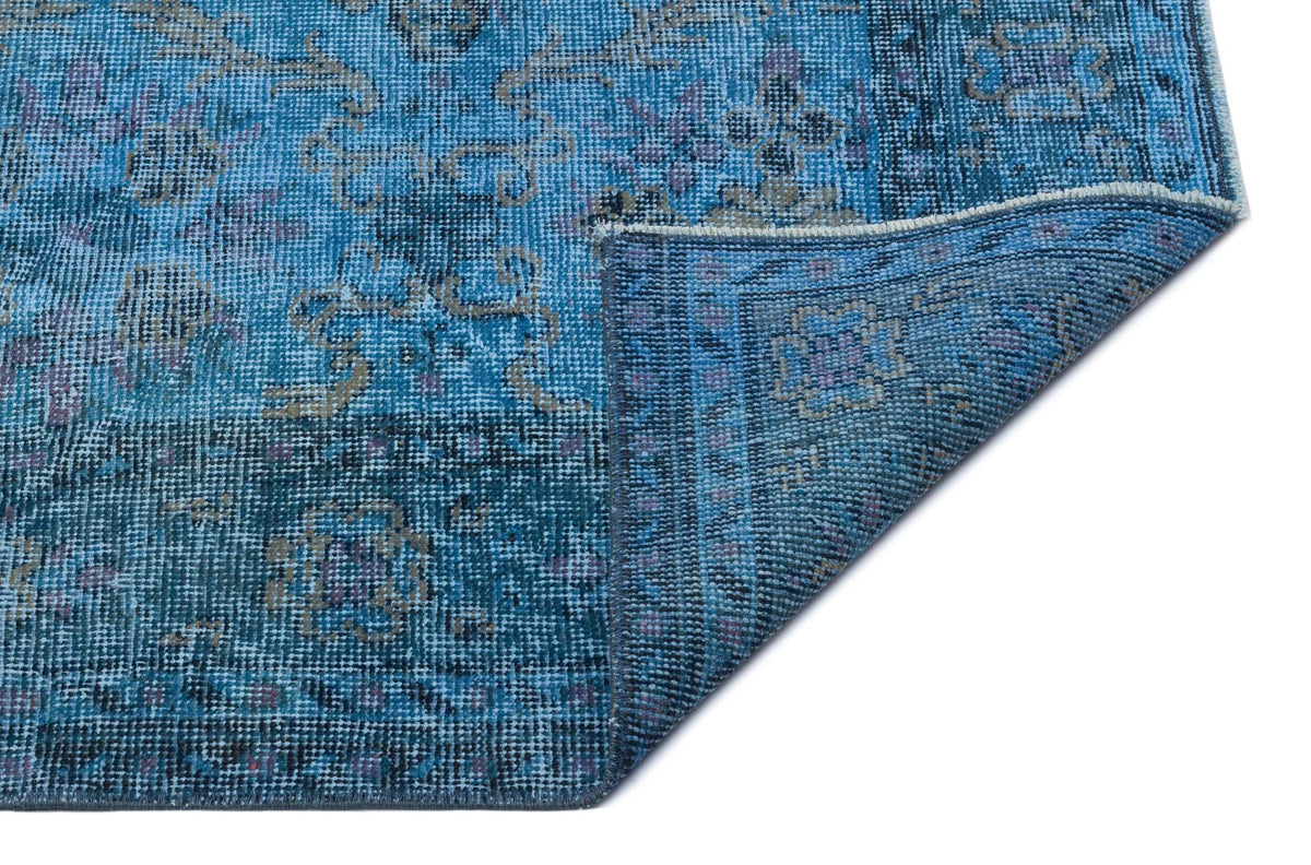 Blue distressed traditional rug with a floral medallion pattern, shown with a corner folded over on a white background.