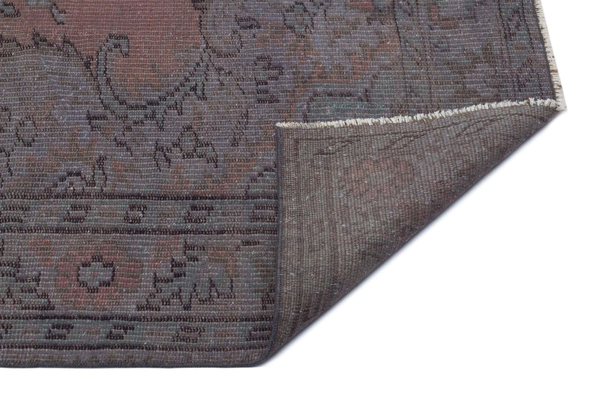 Distressed charcoal and muted plum rug with a traditional floral medallion pattern, showing the woven backing.