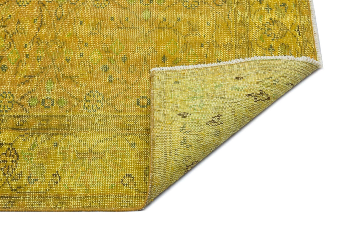 Mustard yellow and green distressed traditional rug with a folded corner showing the woven backing.