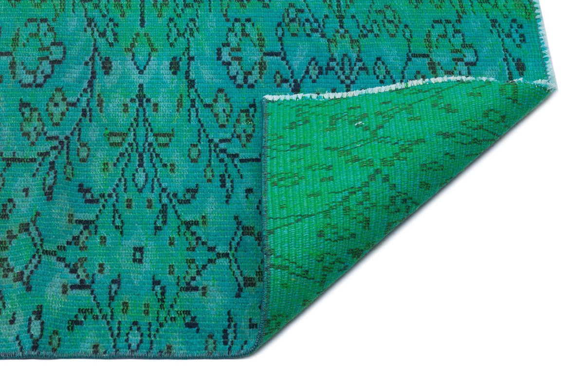Teal and black distressed floral pattern rug with a folded corner revealing the bright green backing.