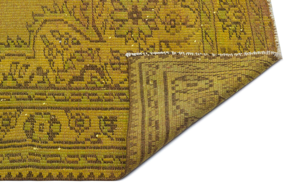 Mustard yellow and brown vintage-style rug with a floral medallion pattern, shown with a folded corner on white.