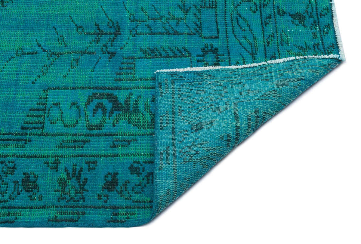 Teal and black distressed rug with a traditional floral medallion pattern, shown with a corner folded over.