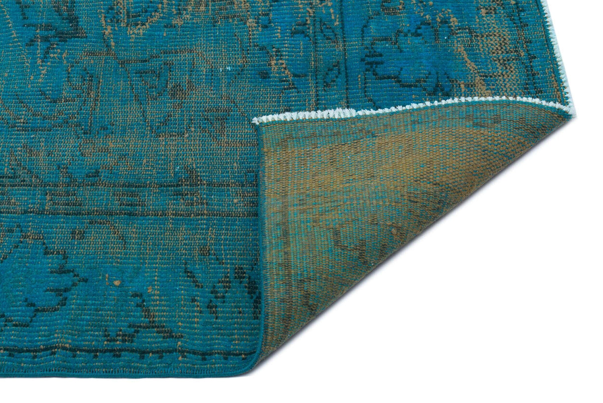 Teal and brown distressed rug with a traditional floral pattern, shown with a corner folded over on a white background.