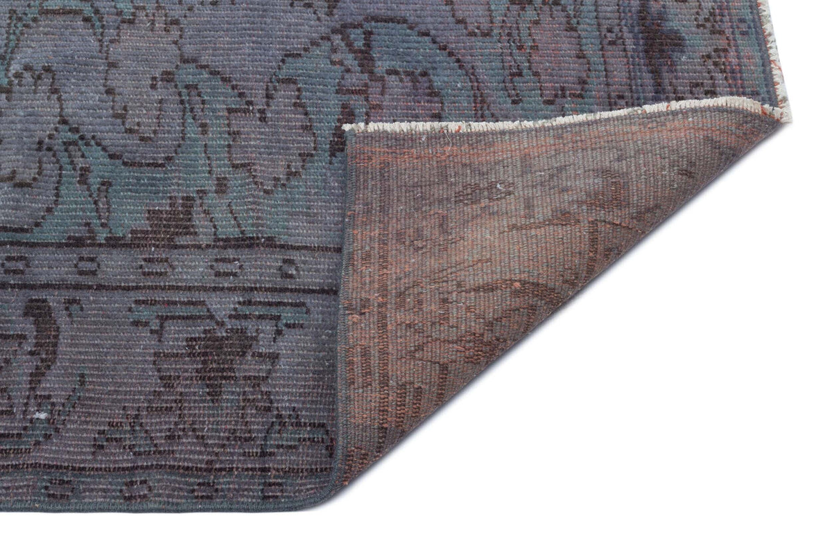 Blue and grey vintage-style rug with a floral medallion pattern, shown with a corner folded to reveal the brown backing.