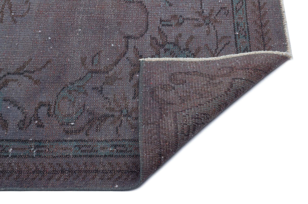Charcoal and teal distressed traditional rug with a floral pattern, shown with a corner folded over on a white background.