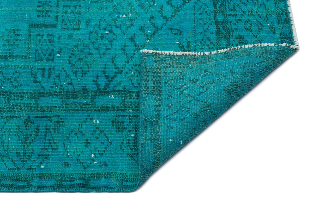 Teal rug with a distressed traditional medallion pattern, shown with a corner folded over on a white background.